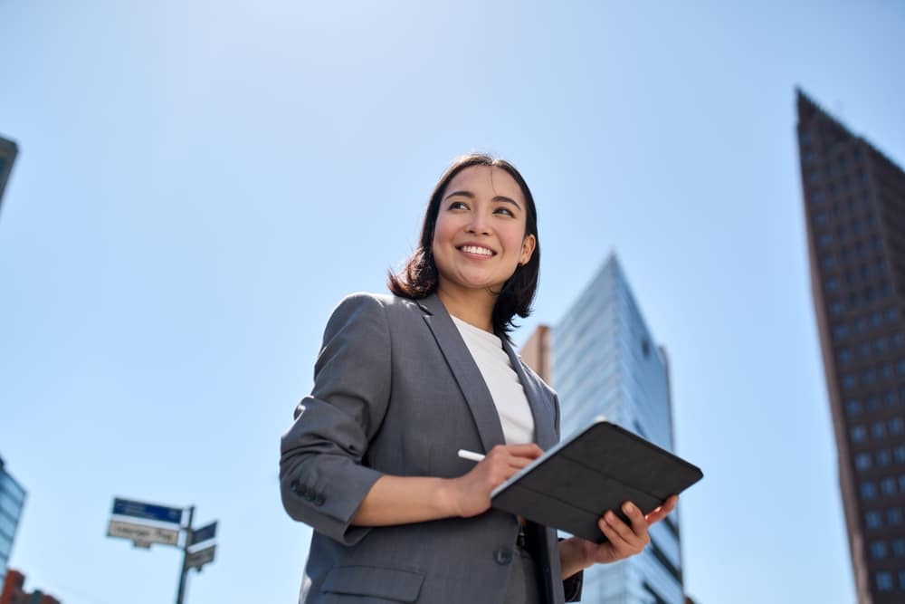 Young female professional, smiling happily in the city, with a tablet.